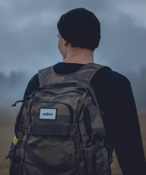 En ung man med camoflague färgad ryggsäck ute i naturen, med profilerad etikett på väskan
