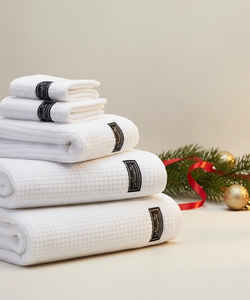 En stapel vita frott&eacute;handdukar med svarta lappar, bredvid en julgranskvist och julgranskulor.