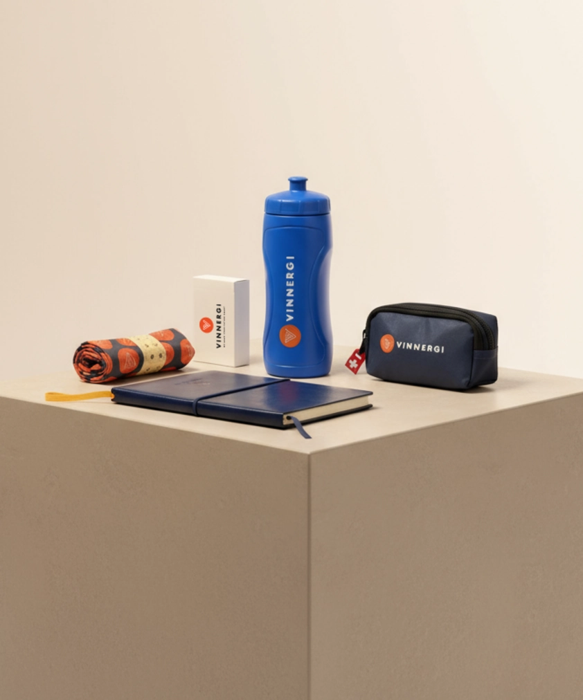En samling Vinnergi-m&auml;rkta f&ouml;rem&aring;l: en bl&aring; vattenflaska, en bl&aring; anteckningsbok, en liten marinbl&aring; p&aring;se och en ihoprullad handduk.