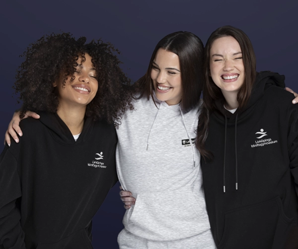 Tre leende kvinnor med armarna om varandra, iklädda jackor med Linköpings logotyp